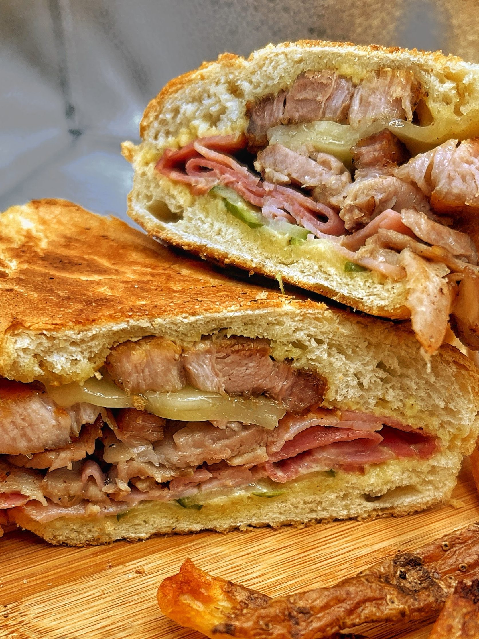 A close-up view of a toasted sandwich filled with assorted meats and cheese, served alongside crispy fries on a wooden cutting board.